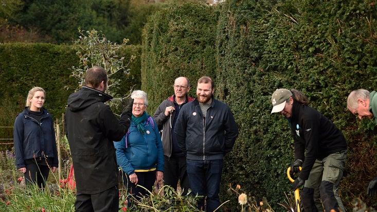 Visitors on a garden tour at Ightham Mote in Kent, talking to garden volunteers.